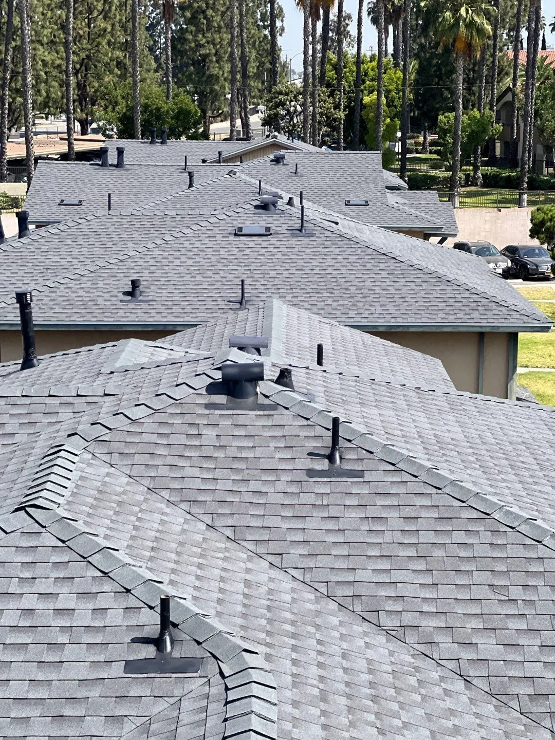 An angled view of a slanted grey-tiled roof with various rooftop elements such as vents and chimneys.